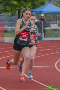 Athlete prepares for pole vault on a track with others watching.