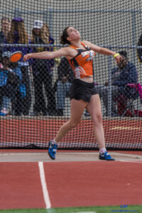 Athlete prepares for pole vault on a track with others watching.
