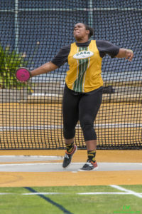 Athlete prepares for pole vault on a track with others watching.