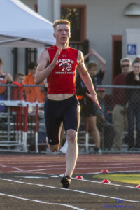 Athlete prepares for pole vault on a track with others watching.