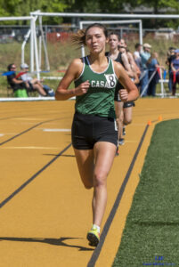 Athlete prepares for pole vault on a track with others watching.