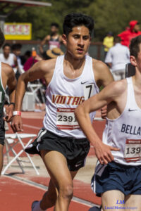 Athlete prepares for pole vault on a track with others watching.