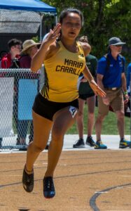 Athlete prepares for pole vault on a track with others watching.