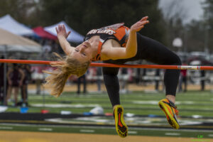 Athlete prepares for pole vault on a track with others watching.