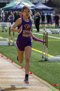 Athlete prepares for pole vault on a track with others watching.