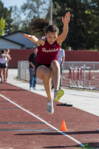 Athlete prepares for pole vault on a track with others watching.