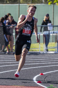 Athlete prepares for pole vault on a track with others watching.