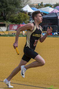 Athlete prepares for pole vault on a track with others watching.