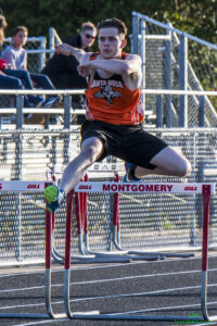 Athlete prepares for pole vault on a track with others watching.