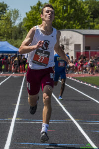 Athlete prepares for pole vault on a track with others watching.