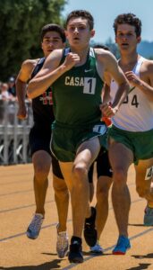 Athlete prepares for pole vault on a track with others watching.