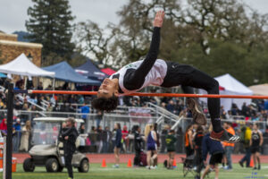 Athlete prepares for pole vault on a track with others watching.