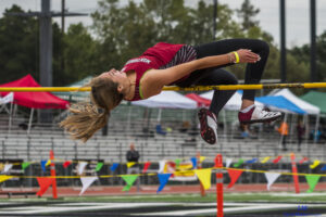 Athlete prepares for pole vault on a track with others watching.