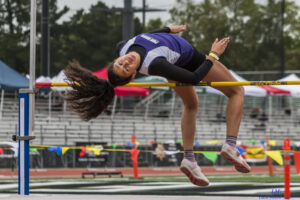 Athlete prepares for pole vault on a track with others watching.