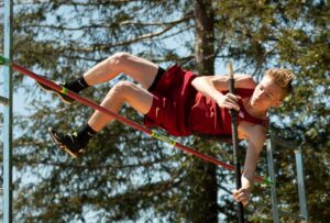 Athlete prepares for pole vault on a track with others watching.