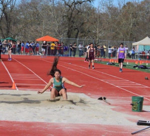 Athlete prepares for pole vault on a track with others watching.