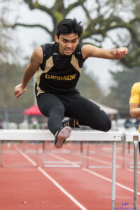 Athlete prepares for pole vault on a track with others watching.