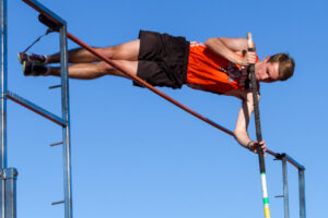 Athlete prepares for pole vault on a track with others watching.