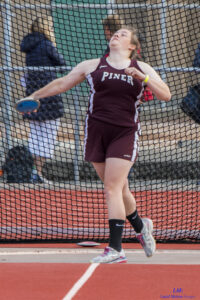Athlete prepares for pole vault on a track with others watching.
