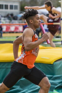 Athlete prepares for pole vault on a track with others watching.