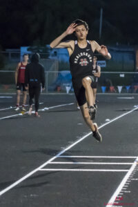 Athlete prepares for pole vault on a track with others watching.