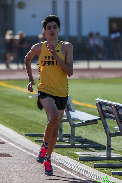 Athlete prepares for pole vault on a track with others watching.