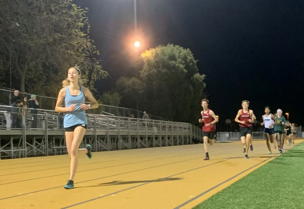 Athlete prepares for pole vault on a track with others watching.