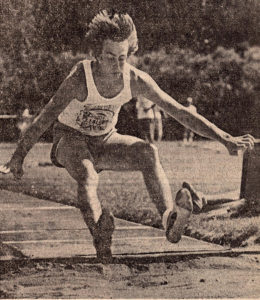 Athlete prepares for pole vault on a track with others watching.