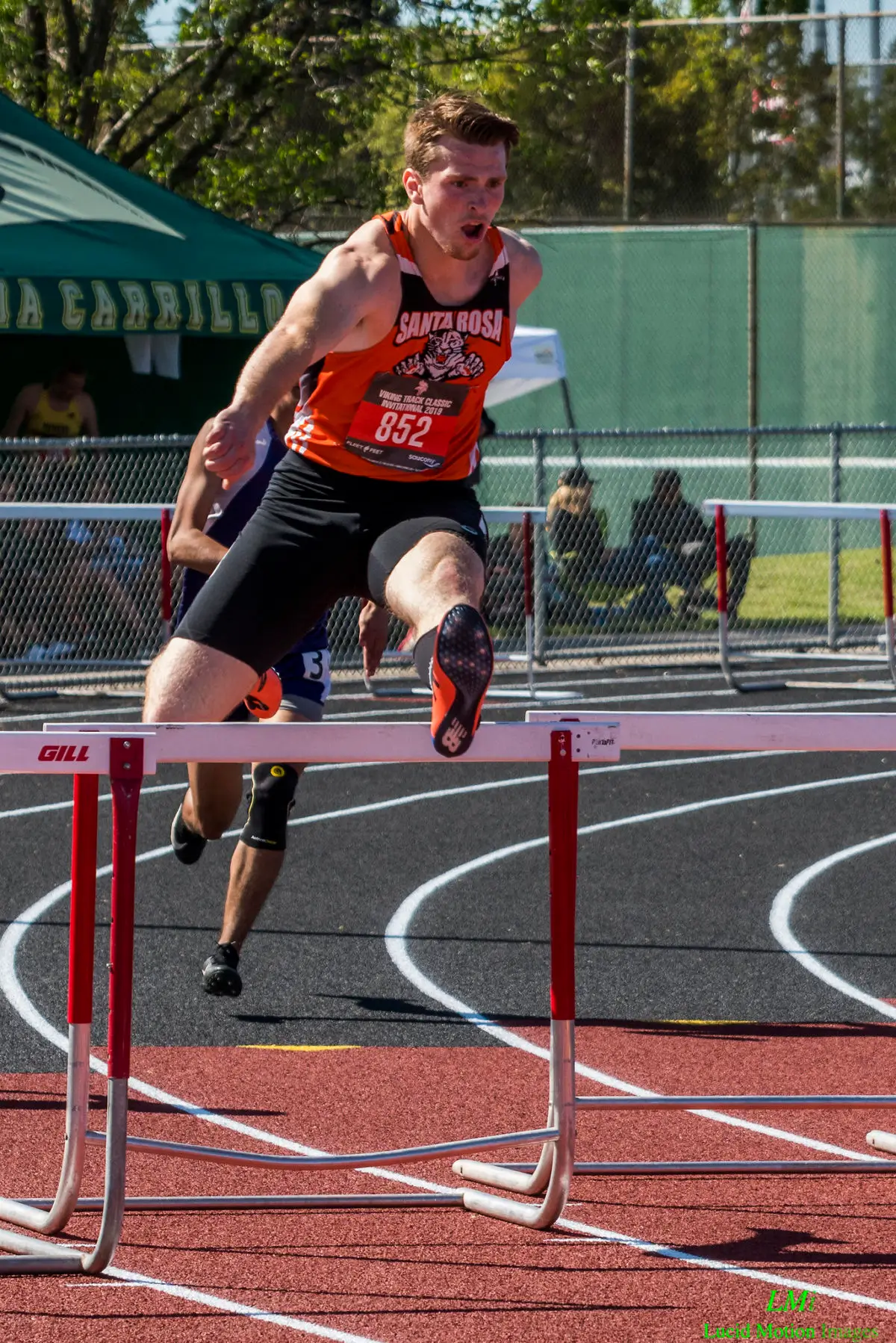 Athlete mid-air hurdling on a track during a race.